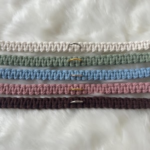 May include: Five macrame cord bracelets in different colors, each with a metal ring. The colors are white, green, blue, pink, and brown.