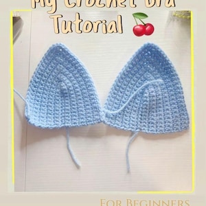 May include: Two light blue crochet bra cups with long yarn tails, displayed on a white surface. The text "My Crochet Bra Tutorial" and "FOR BEGINNERS" are visible. A pair of cherries is also shown.