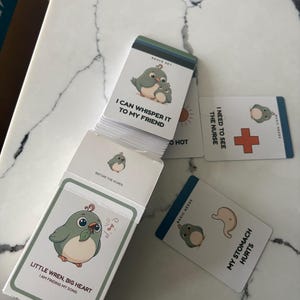 May include: A deck of communication cards featuring cartoon birds and text. The top card reads I CAN WHISPER IT TO MY FRIEND. Other visible cards include I NEED TO SEE THE NURSE with a red cross, MY STOMACH HURTS with a stomach icon, and LITTLE WREN, BIG HEART.