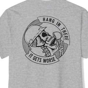 May include: Gray t-shirt with a black and white graphic of a skeleton wearing a hard hat and holding a mug. The graphic says "Hang in there, it gets worse".