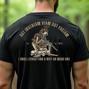 Puede incluir: Camiseta negra con un gráfico de un soldado esqueleto sosteniendo un rifle y sentado sobre una pila de cráneos. El texto "Aut Inveniam Viam Aut Faciam" está por encima del gráfico y el texto "I shall either find a way or make one" está por debajo del gráfico.