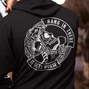 Puede incluir: Sudadera con capucha negra con un estampado gráfico blanco de un esqueleto sosteniendo herramientas. El gráfico dice "Hang in there, it gets worse".