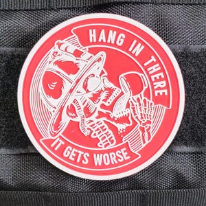 May include: Red and white embroidered patch with a skull wearing a firefighter's helmet and holding a phone. The text reads "Hang in there it gets worse".