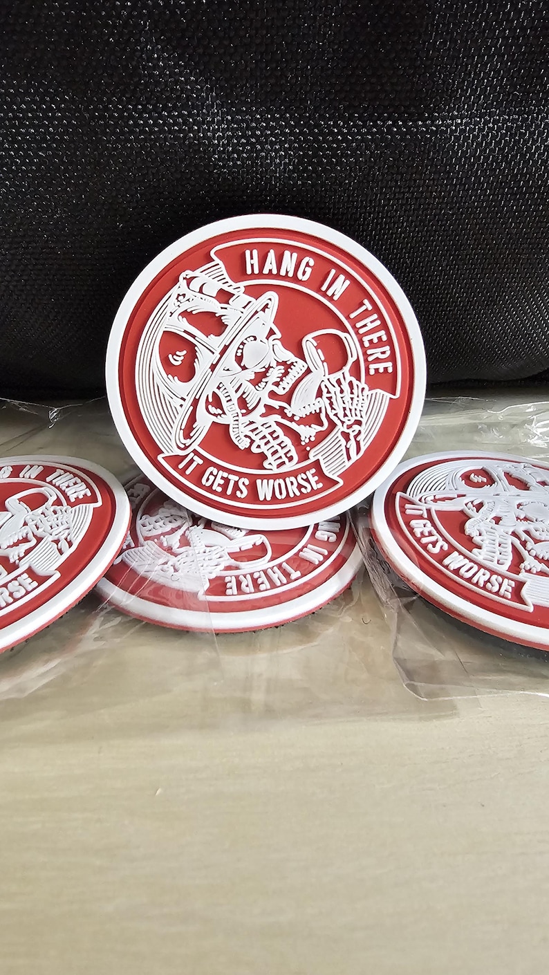 May include: Four red and white round patches with a skull and crossbones design. The text on the patches reads "Hang in there, it gets worse".