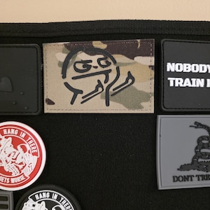 Può includere: Una collezione di toppe con vari disegni. Una toppa presenta un'illustrazione in stile meme con un gesto del dito medio. Altre toppe includono testo come "NOBODY TRAIN" e "DON'T TRE". Le toppe sono in vari colori e forme.