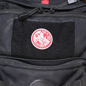 May include: A black backpack with a red zipper and a red and white patch that says "Hang in there it gets worse".