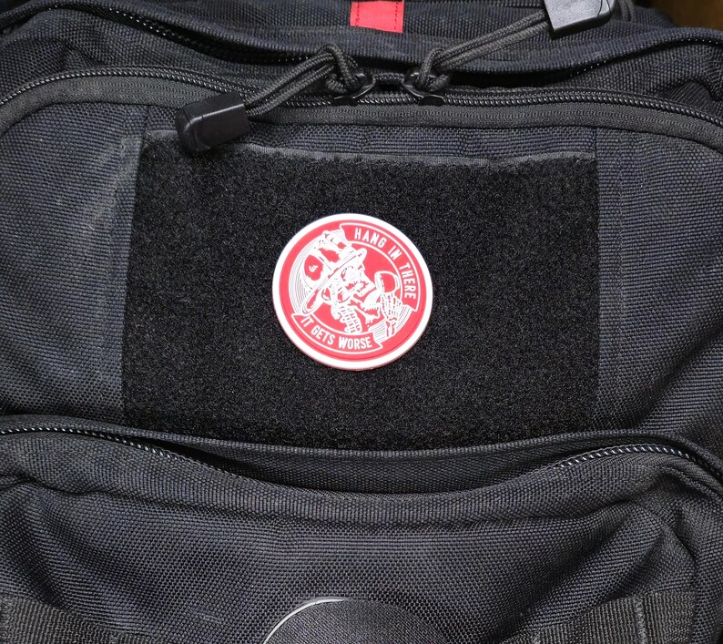 May include: A black backpack with a red zipper and a red and white patch that says "Hang in there it gets worse".
