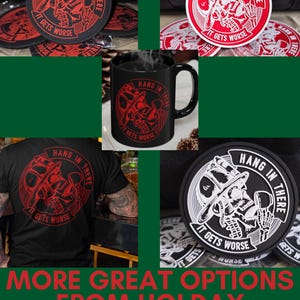 May include: A set of four black coasters with a white skull design and the text "Hang in there, it gets worse". The coasters are shown on a green surface. A black mug with the same design is also shown. A black t-shirt with the same design is shown on a person.