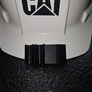 May include: A black plastic safety helmet brim attachment with a ridged design.