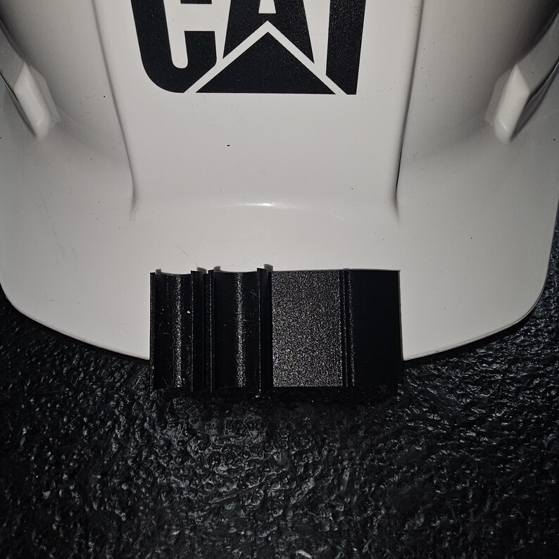 May include: A black plastic safety helmet brim attachment with a ridged design.
