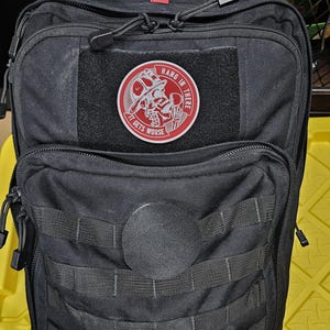 May include: Black tactical backpack with a red and white patch that says "Hang in there, it gets worse". The patch features a skull wearing a firefighter helmet.