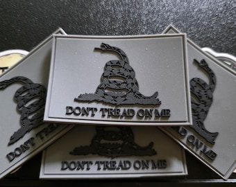 May include: Several gray patches with a black rattlesnake and the text "DON'T TREAD ON ME". The patches are rectangular with a white border. The image shows a close-up of the patches.