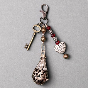 Purse charm keychain with red, silver, and bronze beads, accented by an antique style key and steampunk charm on a silver lobster claw