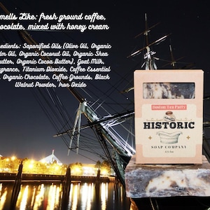 May include: A bar of soap in a box with the text "Boston Tea Party" and "Historic Soap Company." The soap is brown and white, with a dark background and a ship in the background. The text says it smells like coffee, chocolate, and honey cream.