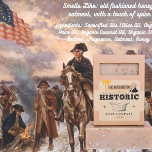 May include: A bar of soap and its box from The Washington Historic Soap Company. The box is light brown with the company name and a picture of George Washington. The soap is light brown and has a rectangular shape. The background is a painting of George Washington on a horse.