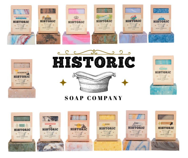 May include: A collection of artisan soaps from the Historic Soap Company. Each soap is packaged in a cardboard box with a label. The soaps are various colors, including blue, pink, green, and yellow. The brand logo features a vintage bathtub.