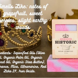 May include: A pink and purple swirled soap bar with a matching box from The Queen Historic Soap Company. The soap is on a pink and purple block. A gold crown is in the background. The soap smells like grapefruit, sweet berries, and earthy woods.