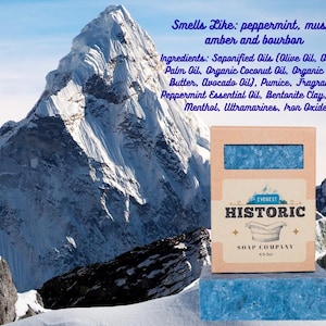 May include: A bar of blue soap and its box, with the text "Everest Historic Soap Company." The box is brown with a blue soap bar visible through a window. The background features a snowy mountain.