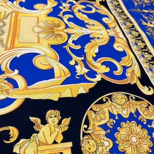 Pode incluir: Um tecido preto e azul com um padrão barroco dourado. O padrão apresenta querubins, motivos florais e detalhes ornamentados.