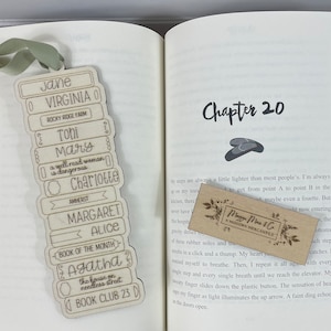 May include: A wooden bookmark with a stack of books engraved on it. The bookmark features the names Jane, Virginia, Tohi, Mary, Charlotte, Margaret, Alice, Agatha, and the text "Book Club 23".