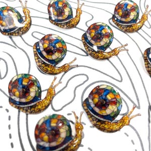 May include: A collection of colorful snail-shaped decorative items. Each snail features a mosaic-style shell with a vibrant array of colors, including blue, yellow, red, and green. The snails have detailed, textured bodies and are set against a white background with gray contour lines.