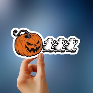 Puede incluir: Una pegatina con una calabaza de Halloween naranja con una sonrisa amenazante, perseguida por tres fantasmas blancos.