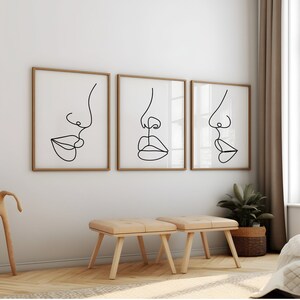 May include: Three framed black and white line drawings of faces with noses and lips. The drawings are in a minimalist style and are hung on a white wall.
