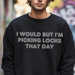 May include: A black sweatshirt with the text "I would but I'm picking locks that day" printed in white.