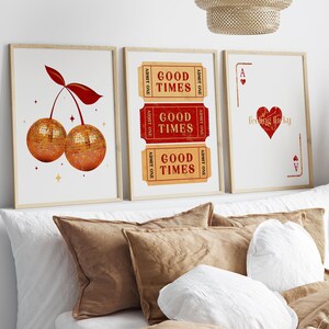 Peut inclure: Trois impressions encadr&eacute;es dans un sch&eacute;ma de couleurs rouge et or. La premi&egrave;re impression repr&eacute;sente une cerise avec des moiti&eacute;s de boule disco. La deuxi&egrave;me impression comporte trois billets qui disent "Good Times". La troisi&egrave;me impression repr&eacute;sente un as de c&oelig;ur rouge avec le texte "feeling lucky".