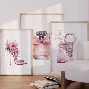 Puede incluir: Tres impresiones enmarcadas con un diseño de acuarela rosa y blanco. Las impresiones muestran un zapato de tacón alto con flores, una botella de perfume y un bolso de mano con diamantes de imitación.