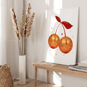Peut inclure: Une impression encadr&eacute;e blanche avec un motif de cerise rouge. La cerise est compos&eacute;e de deux boules disco. L'arri&egrave;re-plan est blanc avec des &eacute;toiles dor&eacute;es.