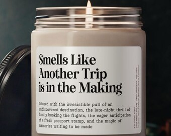 May include: A beige scented candle in a clear glass jar with a black lid. The white label features the text: Smells Like Another Trip is in the Making, followed by descriptive text about the pull of an undiscovered destination and travel.