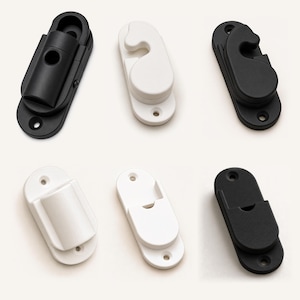 May include: A collection of six oval-shaped window sash locks and mounting brackets in matte black and white finishes. Each piece features a central mounting hole at the top and bottom, with varying mechanical latch designs for securing window frames.