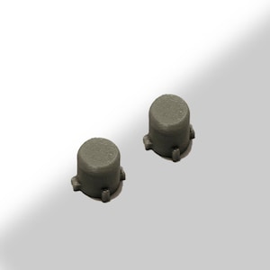 May include: Two small, cylindrical, gray objects with a flat top and three small protrusions at the base. The objects are evenly spaced and appear to be made of a solid material, possibly plastic or metal. The background is a gradient of white to light gray.