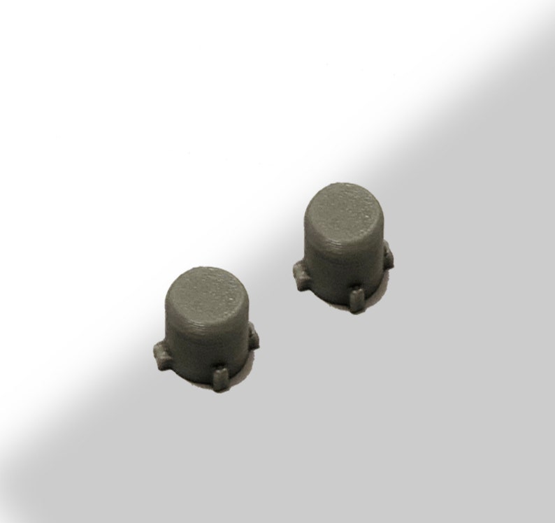 May include: Two small, cylindrical, gray objects with a flat top and three small protrusions at the base. The objects are evenly spaced and appear to be made of a solid material, possibly plastic or metal. The background is a gradient of white to light gray.