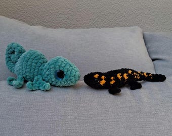 May include: Two crocheted stuffed animals, a green chameleon and a black and orange salamander, on a gray couch.