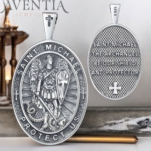 May include: Silver pendant featuring Saint Michael the Archangel. The front of the pendant shows Saint Michael standing on a snake, holding a sword and shield. The back of the pendant has the inscription "Saint Michael the Archangel Be Our Shield and Protector".