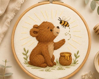 May include: A circular wooden embroidery hoop containing a fabric panel with a hand-stitched design of a brown bear sitting next to a small honey pot. A bee is embroidered above the bear, surrounded by stitched yellow sunburst rays and green grass.
