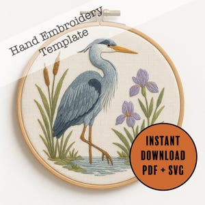Peut inclure: Modèle de broderie à la main représentant un héron bleu dans l'eau, entouré d'iris violets et de roseaux, dans un cercle de broderie en bois. Le texte indique "Hand Embroidery Template" et "Instant Download PDF + SVG".