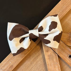 May include: A brown and white cow print bow tie. The bow tie is made of fabric and has a simple design.