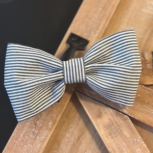 May include: A white and black striped bow tie. The bow tie is made of a fabric with a subtle texture.