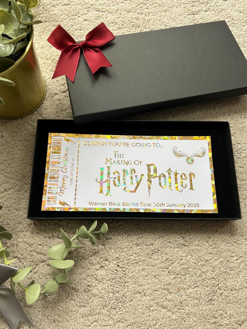 May include: A golden ticket with a holographic finish, reading "OLIVER!! YOU'RE GOING TO... THE MAKING OF HARRY POTTER Warner Bros. Studio Tour. 30th January 2025". The ticket is in a black box with a red bow.