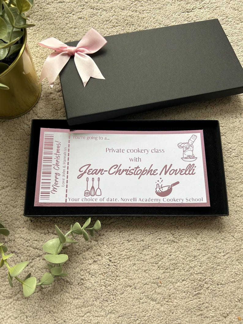 K&ouml;nnte beinhalten: Eine schwarze rechteckige Geschenkbox mit einer hellrosa Schleife auf dem Deckel. Im Inneren befindet sich ein rechteckiger Gutschein mit dem Text: Merry Christmas! Love John & Hannah xx, You're going to a... Private cookery class with Jean-Christophe Novelli.