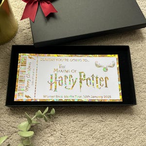 May include: A gold and white ticket with the text "OLIVER!! YOU'RE GOING TO... THE MAKING OF Harry Potter Warner Bros. Studio Tour. 30th January 2025" and a graphic of a golden snitch.