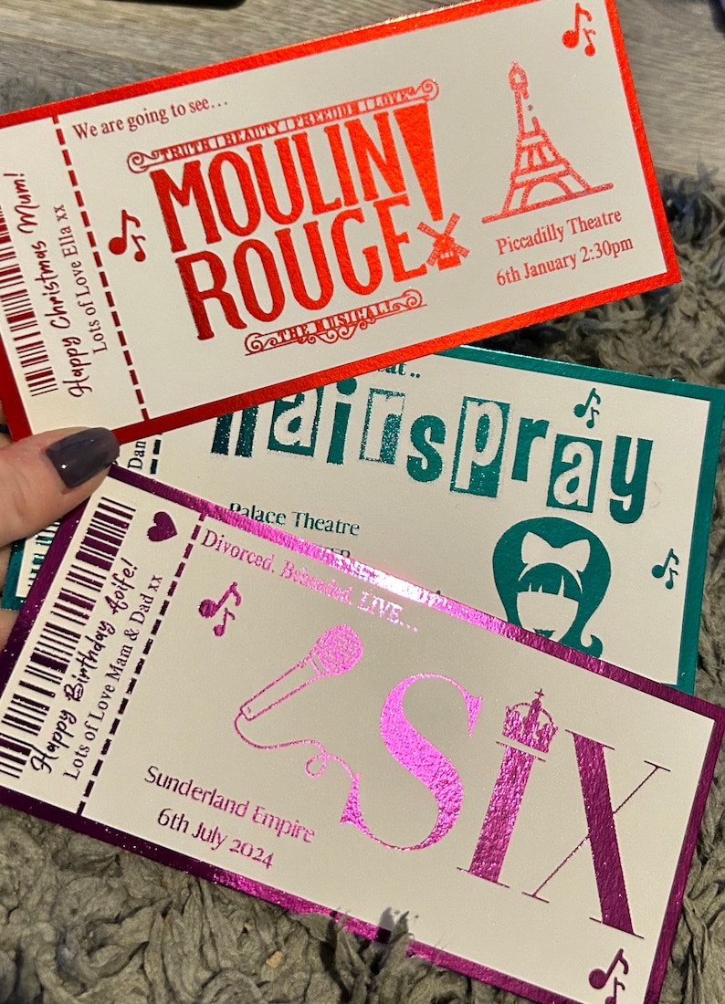 K&ouml;nnte beinhalten: Drei rechteckige Theatertickets mit metallischer Folienbeschriftung und Grafiken. Das oberste Ticket ist rot f&uuml;r Moulin Rouge, das mittlere ist blaugr&uuml;n f&uuml;r Hairspray und das untere ist lila f&uuml;r Six. Jedes Ticket enth&auml;lt einen Strichcode, Noten und Veranstaltungsdetails.
