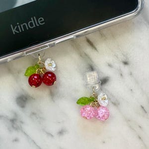 May include: Two beaded charms with gold-colored findings. One charm features two red beads with green leaves and white flowers. The other charm has two pink beads with green leaves and white flowers. The word "kindle" is visible.