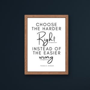 May include: A framed print with the quote "CHOOSE THE HARDER Right INSTEAD OF THE EASIER wrong" by Thomas S. Monson. The text is in black against a white background, within a brown wooden frame. A digital download graphic is in the bottom right.