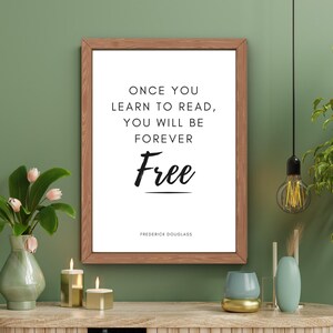 May include: A framed print with a white background and black text that reads "Once you learn to read, you will be forever Free" with the name "Frederick Douglass" at the bottom. The print is hanging on a green wall with a wooden frame.