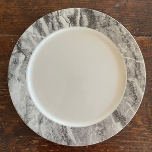 May include: A white ceramic dinner plate with a gray marble pattern around the edge.