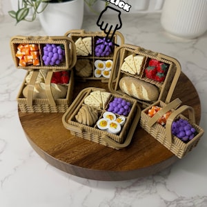 May include: Miniature picnic baskets filled with food items, including grapes, cheese, bread, and fruit. The baskets are made of a light brown material and are arranged on a wooden tray. The word "CLICK" is visible in the image.